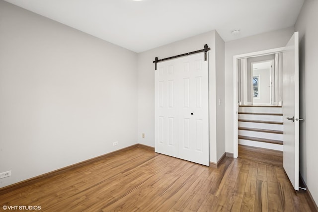 unfurnished bedroom with a barn door, a closet, and light hardwood / wood-style floors