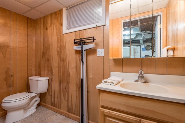 bathroom featuring toilet, wood walls, vanity, and a drop ceiling