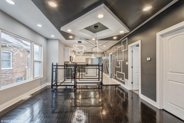 hallway with a raised ceiling, a chandelier, and dark wood-type flooring