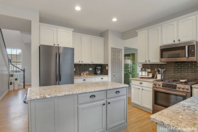 kitchen with decorative backsplash, light stone countertops, white cabinetry, and stainless steel appliances