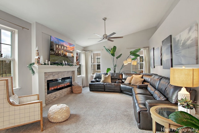 carpeted living room featuring ceiling fan, a healthy amount of sunlight, a stone fireplace, and vaulted ceiling