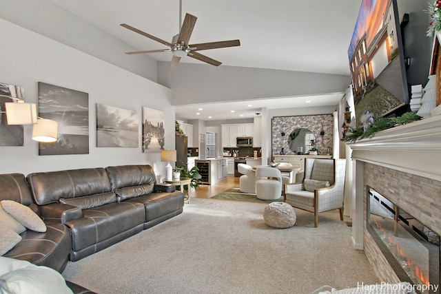 carpeted living room with high vaulted ceiling, beverage cooler, a stone fireplace, and ceiling fan