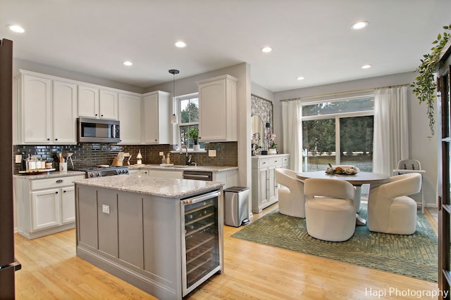 kitchen with pendant lighting, light hardwood / wood-style floors, white cabinetry, stainless steel appliances, and beverage cooler