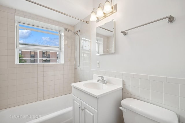 full bathroom featuring tiled shower / bath, vanity, tile walls, and toilet