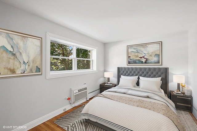 bedroom featuring a wall unit AC, hardwood / wood-style floors, and a baseboard heating unit