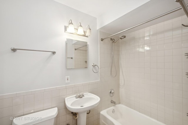 full bathroom featuring sink, tiled shower / bath, tile walls, and toilet