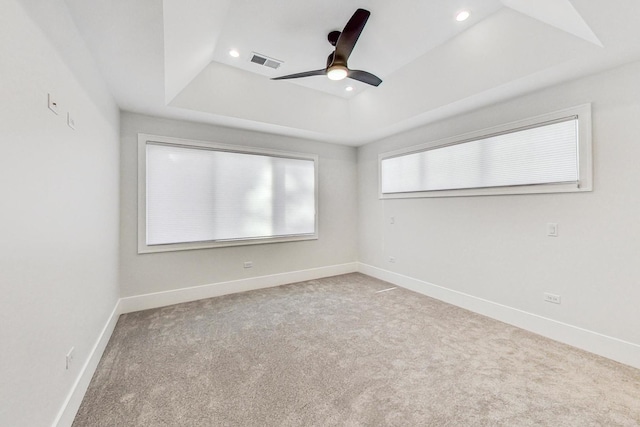 carpeted spare room with a tray ceiling and ceiling fan