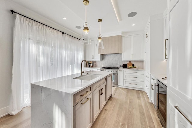 kitchen featuring light stone countertops, sink, stainless steel stove, hanging light fixtures, and an island with sink