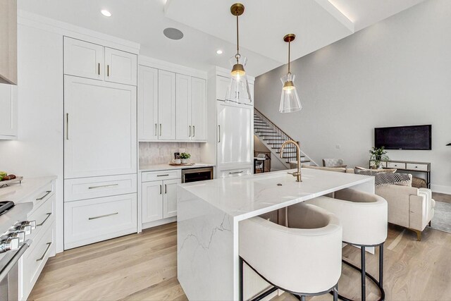 kitchen with white cabinets, stainless steel range with gas cooktop, hanging light fixtures, light wood-type flooring, and light stone counters