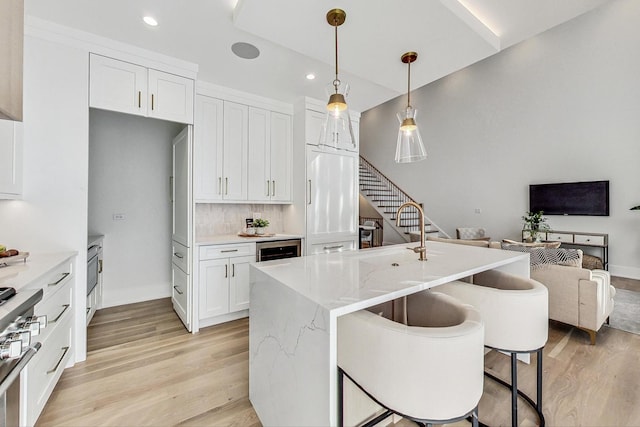 kitchen featuring light stone countertops, backsplash, pendant lighting, light hardwood / wood-style floors, and white cabinets