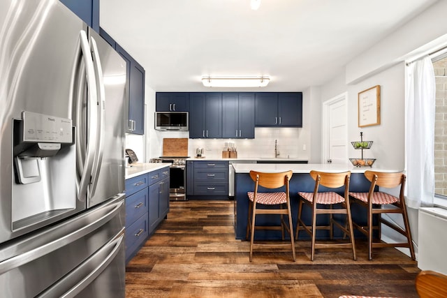 kitchen with a kitchen bar, blue cabinetry, appliances with stainless steel finishes, and dark wood-type flooring