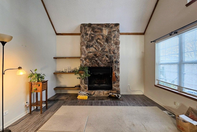 living room with a healthy amount of sunlight, dark hardwood / wood-style floors, a stone fireplace, and lofted ceiling