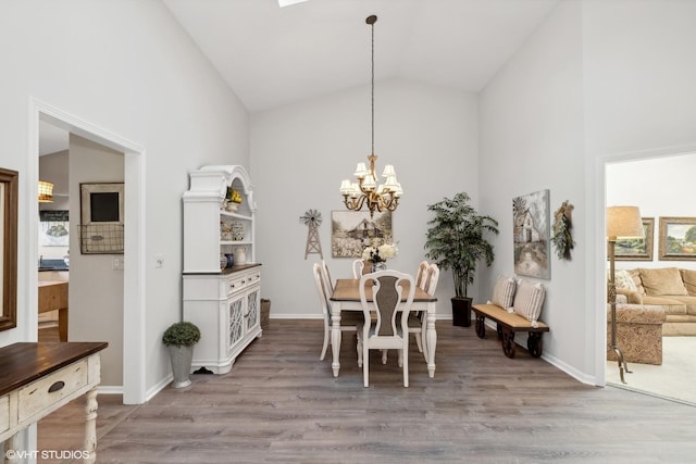 dining area with light wood-type flooring, high vaulted ceiling, and a notable chandelier