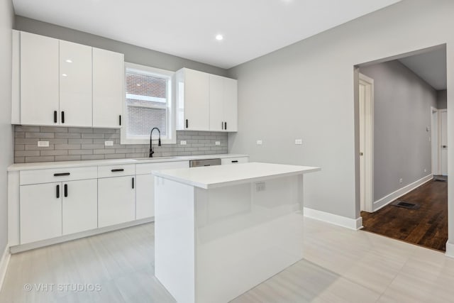 kitchen with sink, white cabinetry, a center island, stainless steel dishwasher, and decorative backsplash