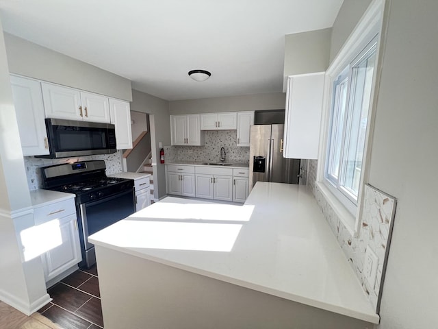 kitchen featuring kitchen peninsula, dark tile patterned floors, appliances with stainless steel finishes, tasteful backsplash, and white cabinetry