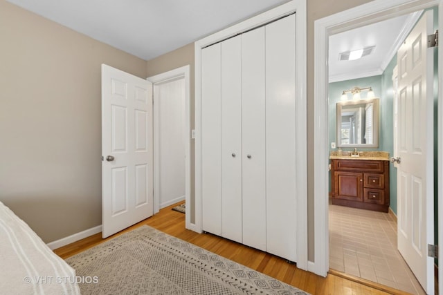 bedroom featuring sink, a closet, ornamental molding, and light wood-type flooring