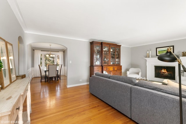 living room with hardwood / wood-style flooring, crown molding, an inviting chandelier, and a brick fireplace