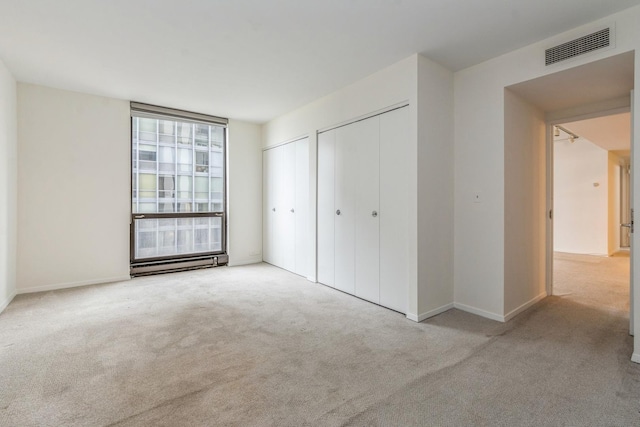 unfurnished bedroom featuring two closets, light carpet, and a baseboard radiator