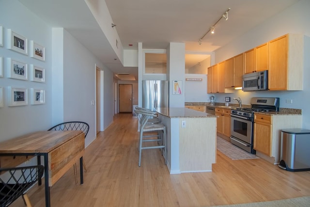 kitchen with light hardwood / wood-style flooring, stainless steel appliances, a kitchen island, and stone countertops