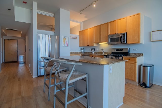 kitchen with a breakfast bar, dark stone countertops, light brown cabinetry, appliances with stainless steel finishes, and light wood-type flooring