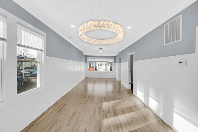 hallway with a healthy amount of sunlight, light hardwood / wood-style floors, and an inviting chandelier