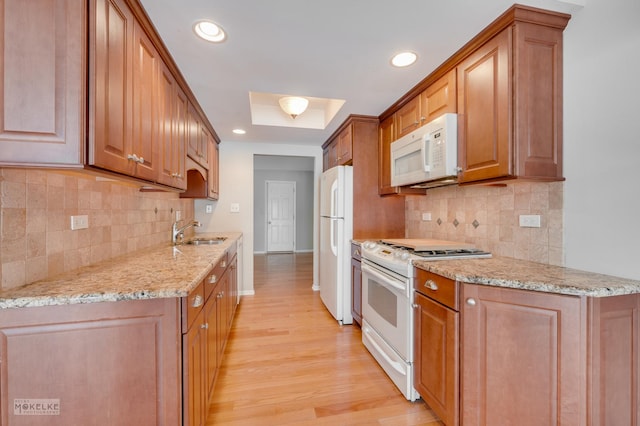 kitchen with light stone counters, white appliances, a raised ceiling, sink, and light hardwood / wood-style flooring