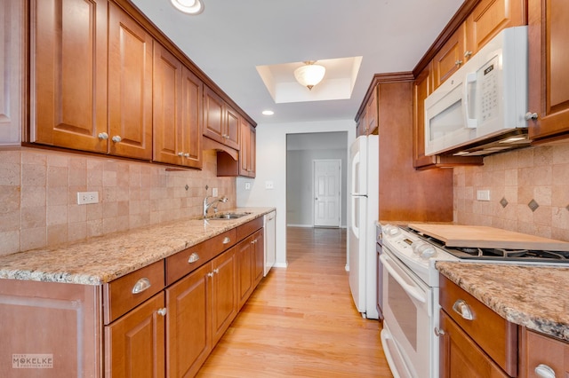 kitchen with light stone countertops, sink, tasteful backsplash, white appliances, and light wood-type flooring