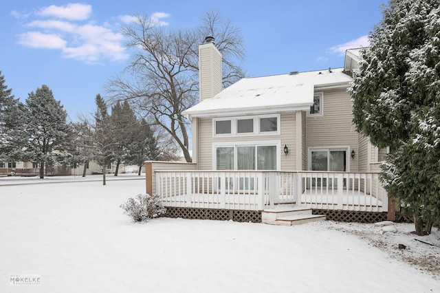 snow covered back of property with a wooden deck