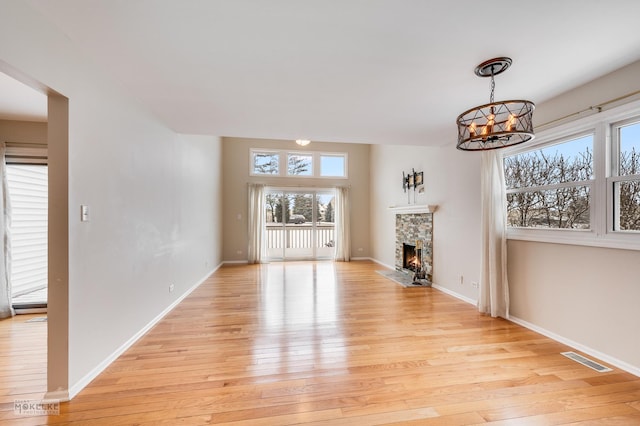 unfurnished living room with a notable chandelier, light wood-type flooring, and a fireplace