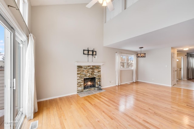 unfurnished living room featuring a towering ceiling, light wood-type flooring, a stone fireplace, and ceiling fan