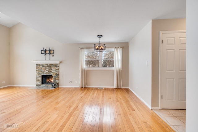 unfurnished living room featuring light hardwood / wood-style floors, a fireplace, and an inviting chandelier