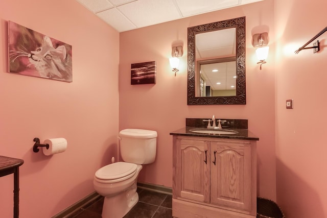 bathroom featuring tile patterned floors, vanity, a drop ceiling, and toilet