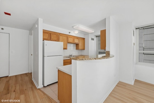 kitchen featuring sink, tasteful backsplash, light hardwood / wood-style flooring, white refrigerator, and kitchen peninsula