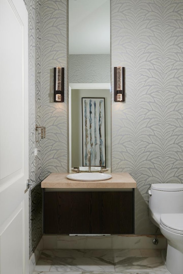 half bath with toilet, marble finish floor, vanity, and wallpapered walls