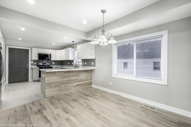 kitchen with decorative light fixtures, tasteful backsplash, kitchen peninsula, stainless steel appliances, and white cabinets