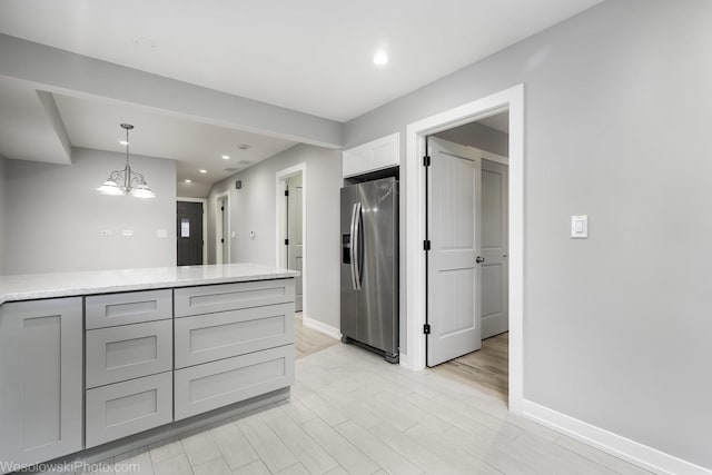 kitchen with stainless steel fridge with ice dispenser, gray cabinetry, a notable chandelier, hanging light fixtures, and light stone counters