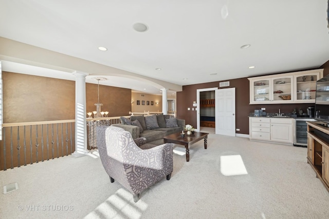 carpeted living room featuring an inviting chandelier, beverage cooler, decorative columns, and wet bar