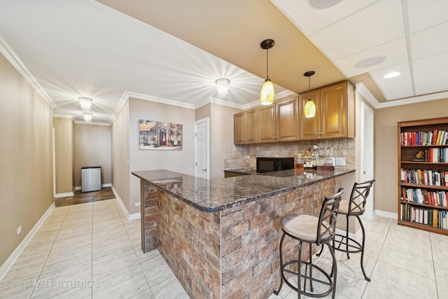 kitchen featuring a kitchen bar, ornamental molding, light tile patterned flooring, kitchen peninsula, and dark stone counters