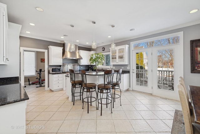 kitchen featuring light tile patterned flooring, decorative light fixtures, white cabinets, crown molding, and wall chimney exhaust hood