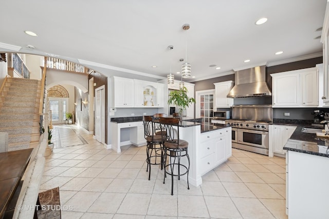 kitchen with wall chimney range hood, appliances with stainless steel finishes, white cabinetry, a center island, and light tile patterned flooring