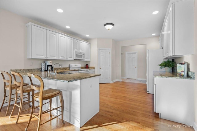 kitchen with white cabinetry, sink, dark stone countertops, kitchen peninsula, and white appliances