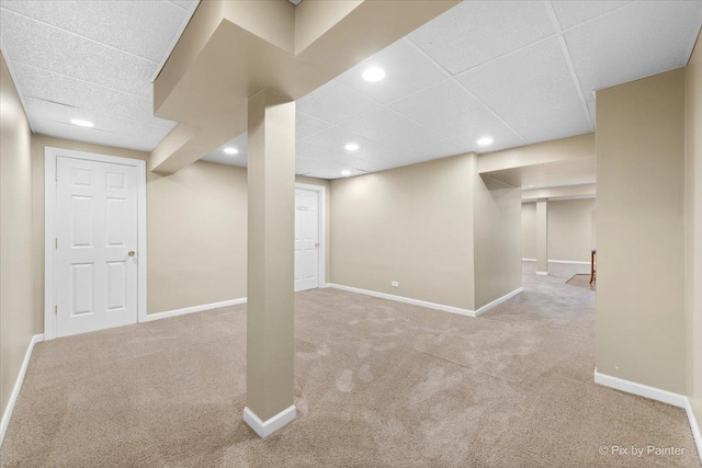 basement with a paneled ceiling and light colored carpet