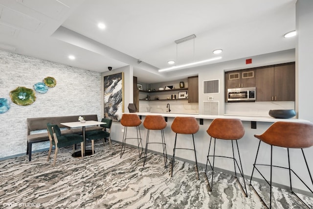 kitchen featuring kitchen peninsula, tasteful backsplash, dark brown cabinetry, sink, and a breakfast bar area