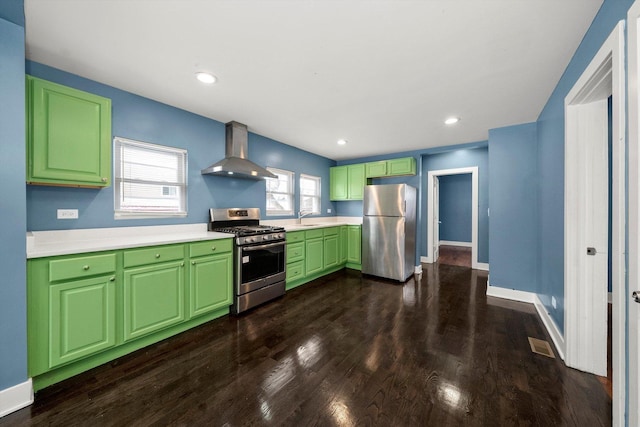 kitchen with green cabinets, wall chimney range hood, sink, appliances with stainless steel finishes, and dark hardwood / wood-style flooring