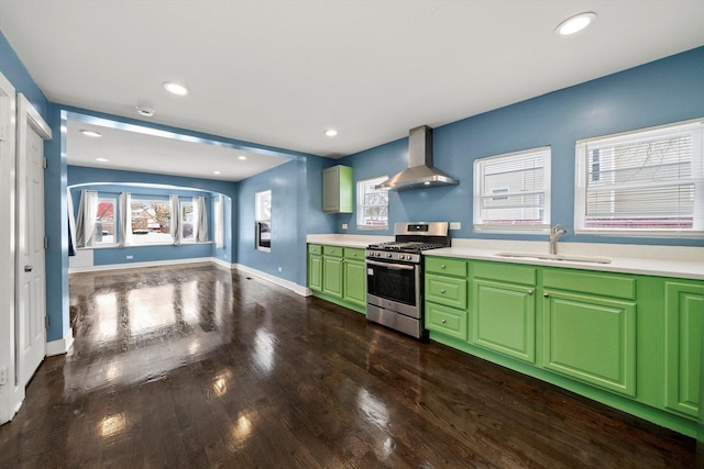 kitchen featuring green cabinets, wall chimney range hood, sink, stainless steel gas stove, and dark hardwood / wood-style flooring