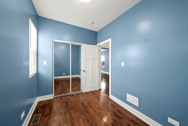 unfurnished bedroom with multiple windows, dark hardwood / wood-style flooring, and a closet