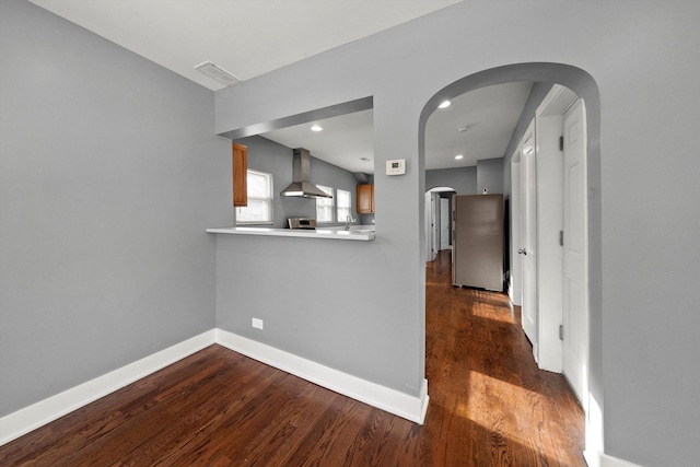 kitchen featuring wall chimney exhaust hood, dark hardwood / wood-style flooring, kitchen peninsula, stainless steel fridge, and range