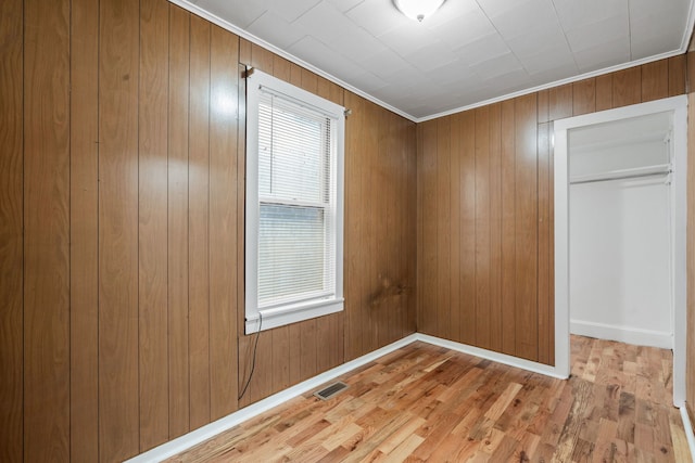 unfurnished bedroom with wooden walls, light hardwood / wood-style floors, a closet, and ornamental molding