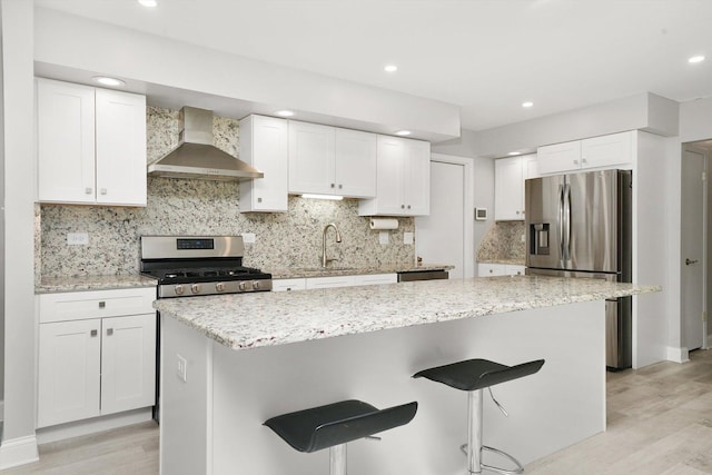 kitchen featuring wall chimney exhaust hood, white cabinetry, a breakfast bar, and appliances with stainless steel finishes