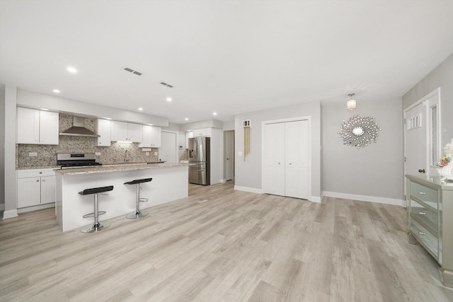 kitchen with appliances with stainless steel finishes, wall chimney exhaust hood, a breakfast bar, a kitchen island, and white cabinetry